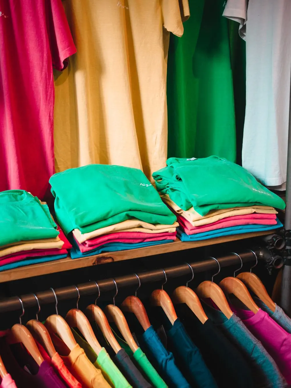 Reference photo 4: folded and hanging coloured T-shirts in a shop — t-shirts we manufacture and export in bulk